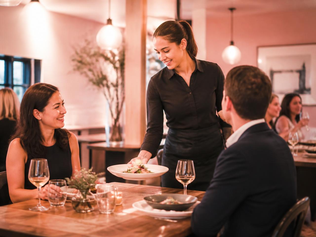 Server presenting a plate to guests in a warm modern restaurant dining room